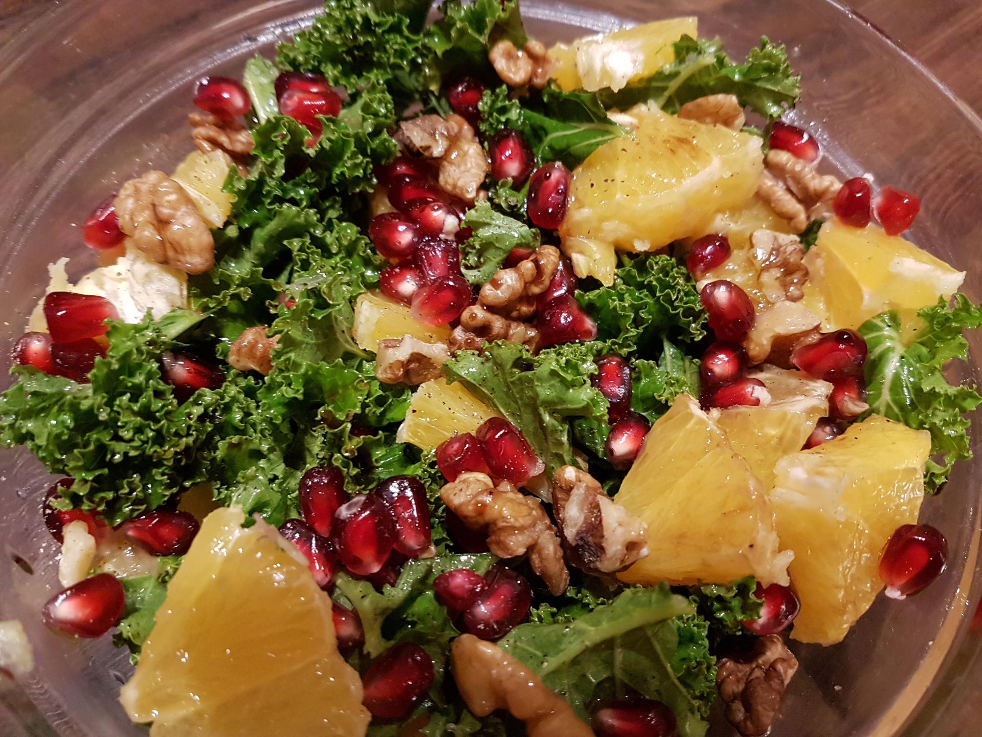 A salad containing curly kale, pomegranate, walnuts and oranges.