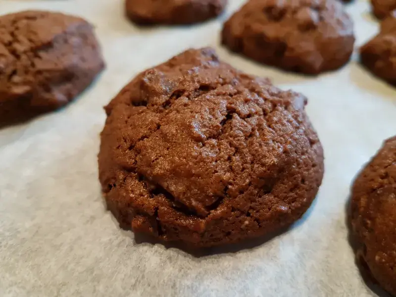 One of a number of stout cookies sitting on baking paper having come out of the oven.